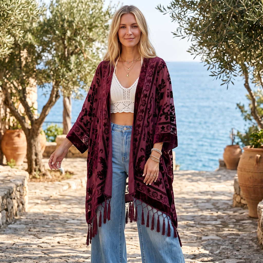RubyLines Burnout Samt Kimono Cardigan in Dunkelrot mit Quasten, getragen von einer Frau vor mediterraner Kulisse.