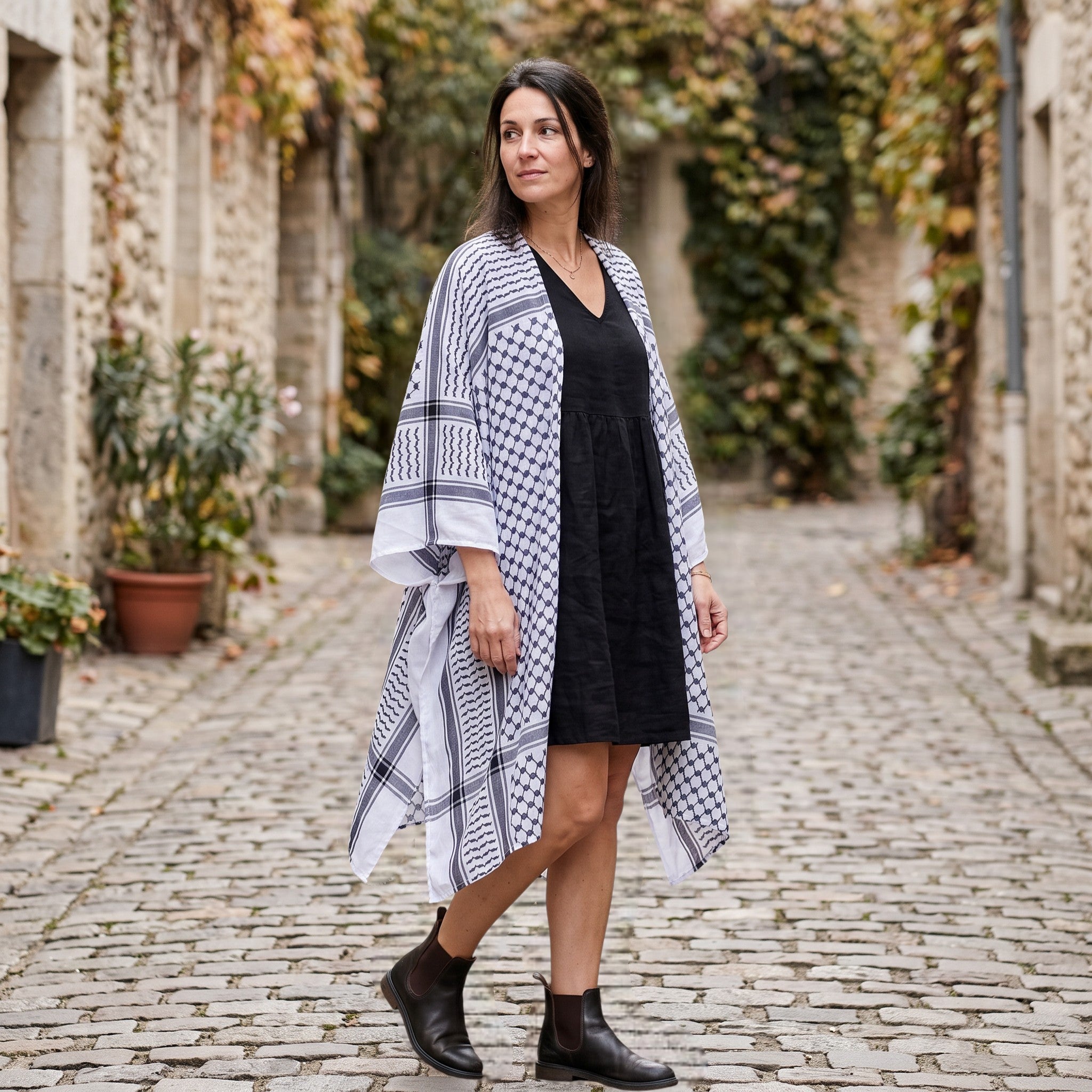 RubyLines langer Cardigan mit Kuffiya-Print in Schwarz-Weiß, getragen von einer Frau in einer historischen Gasse.