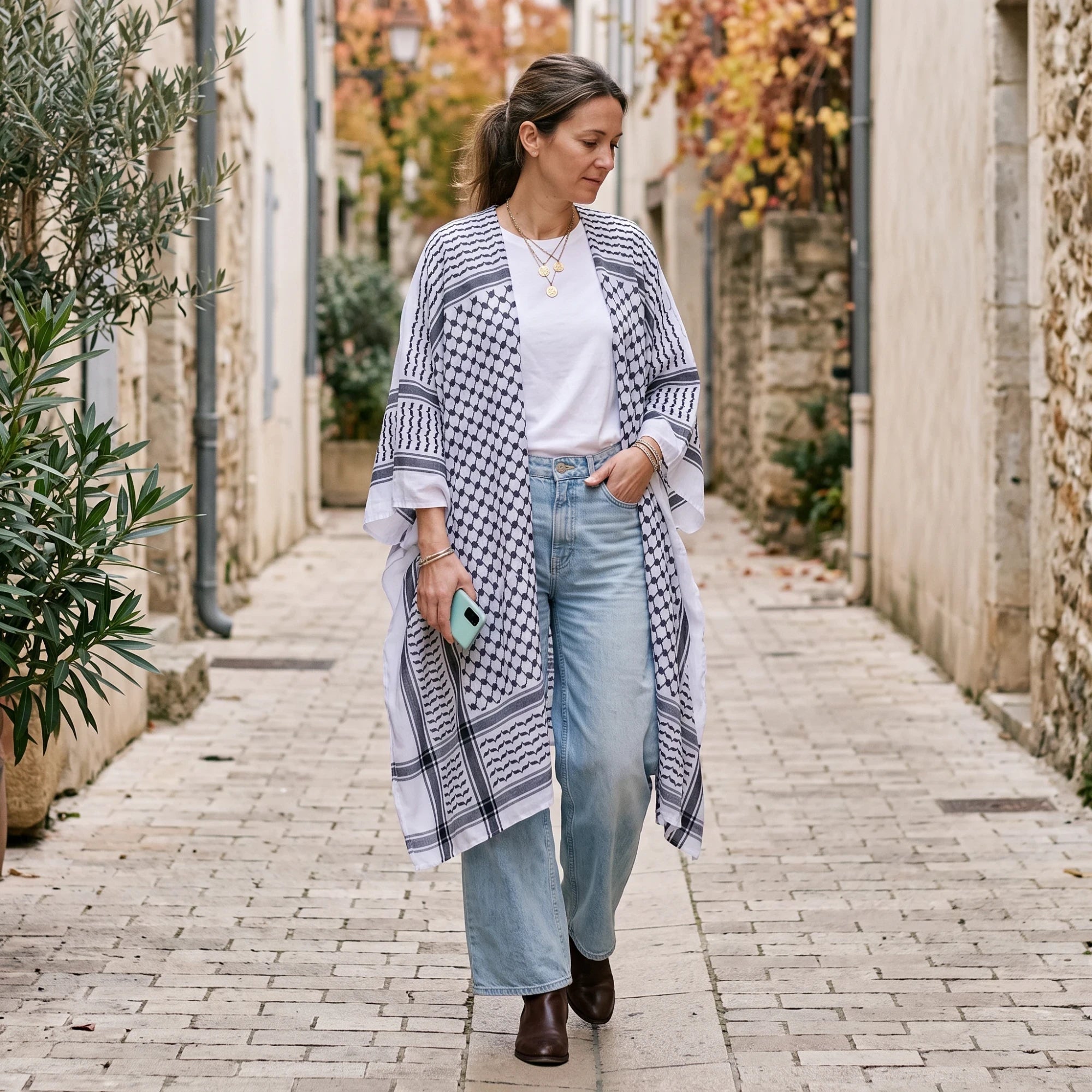 RubyLines langer Cardigan mit Kuffiya-Print in Schwarz-Weiß, getragen von einer Frau in einer Gasse.
